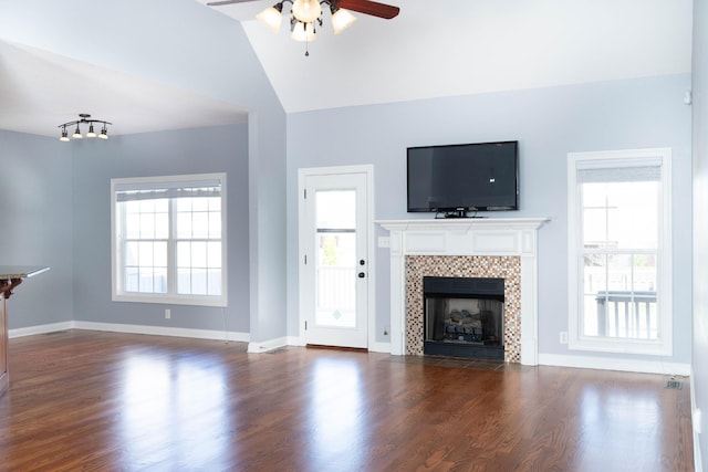 unfurnished living room with lofted ceiling, a ceiling fan, baseboards, a tiled fireplace, and dark wood finished floors