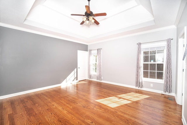 empty room with baseboards, a tray ceiling, and wood finished floors