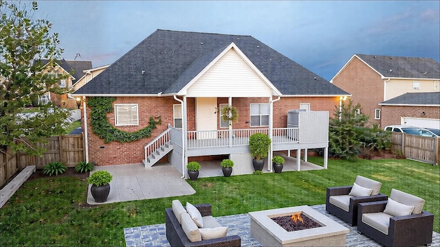 back of property with an outdoor living space with a fire pit, brick siding, a patio, a lawn, and fence