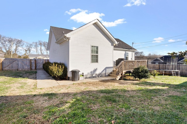 back of house with a trampoline, a wooden deck, a lawn, and a patio