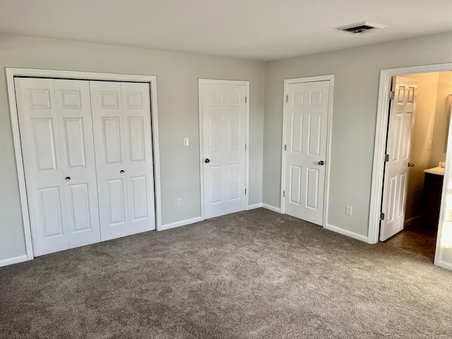 unfurnished bedroom with multiple closets, dark carpet, and ensuite bath