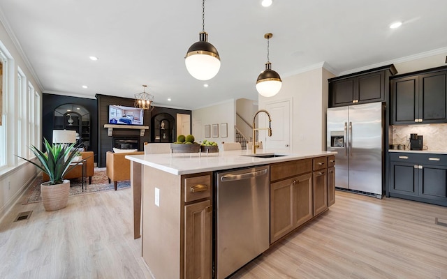 kitchen with an island with sink, stainless steel appliances, a fireplace, light hardwood / wood-style flooring, and sink