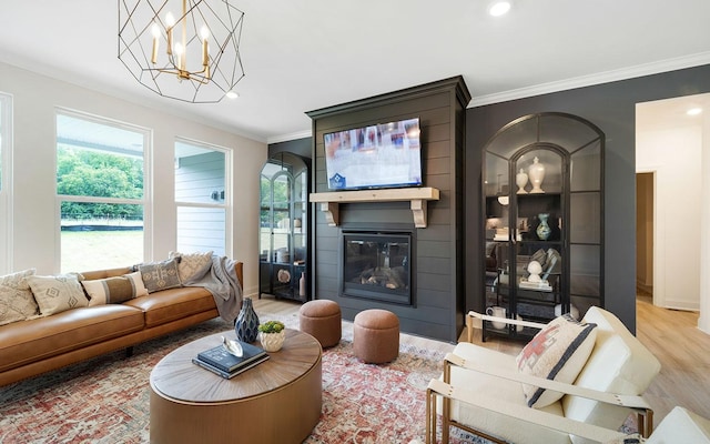 living room with ornamental molding, light hardwood / wood-style floors, a fireplace, and a notable chandelier