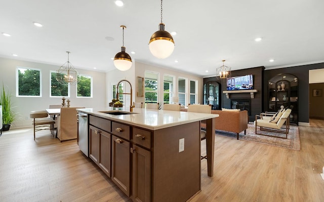 kitchen featuring decorative light fixtures, an island with sink, sink, a large fireplace, and light hardwood / wood-style flooring