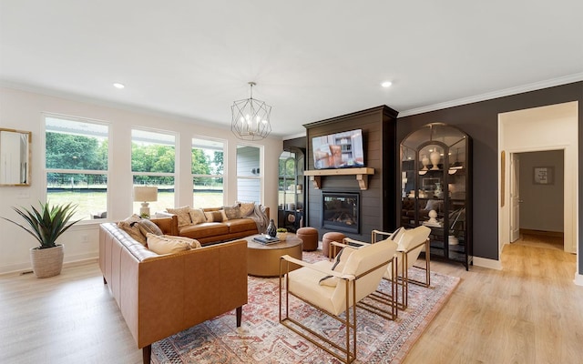 living room featuring light hardwood / wood-style floors, a large fireplace, crown molding, and an inviting chandelier