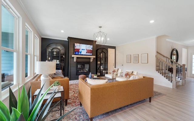 living room featuring light wood-type flooring, a fireplace, crown molding, and a notable chandelier