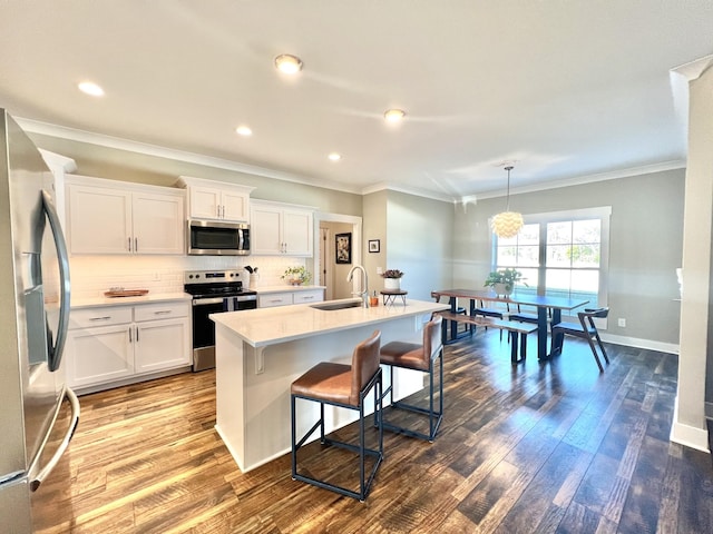 kitchen featuring pendant lighting, white cabinets, stainless steel appliances, sink, and a center island with sink