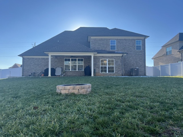 rear view of property featuring a lawn, an outdoor fire pit, and cooling unit