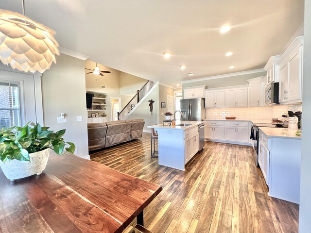 kitchen featuring a center island with sink, stainless steel appliances, wood-type flooring, white cabinets, and a breakfast bar