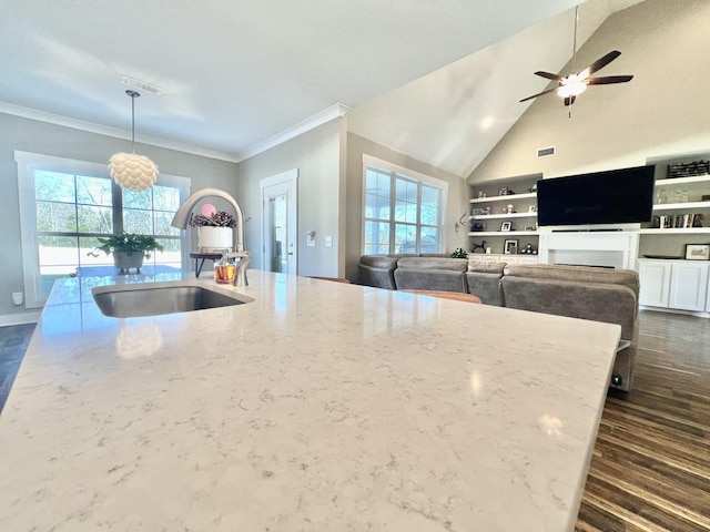 kitchen with pendant lighting, a wealth of natural light, lofted ceiling, sink, and light stone counters