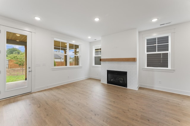 unfurnished living room with a brick fireplace and light hardwood / wood-style flooring