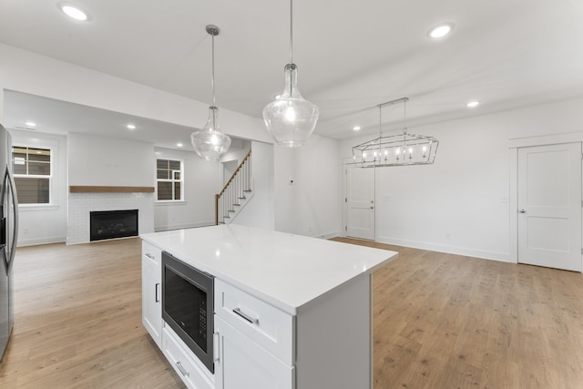 kitchen featuring light wood-type flooring, a kitchen island, built in microwave, and hanging light fixtures