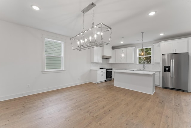 kitchen with appliances with stainless steel finishes, white cabinets, pendant lighting, light hardwood / wood-style flooring, and a center island