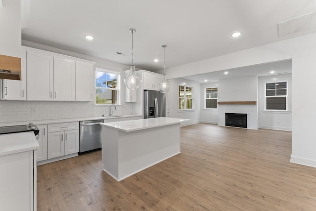 kitchen featuring white cabinetry, appliances with stainless steel finishes, hanging light fixtures, a kitchen island, and sink