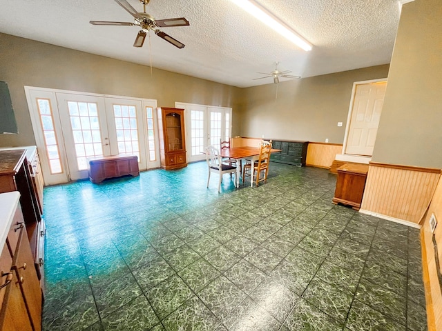 dining area featuring ceiling fan, french doors, wood walls, and a textured ceiling