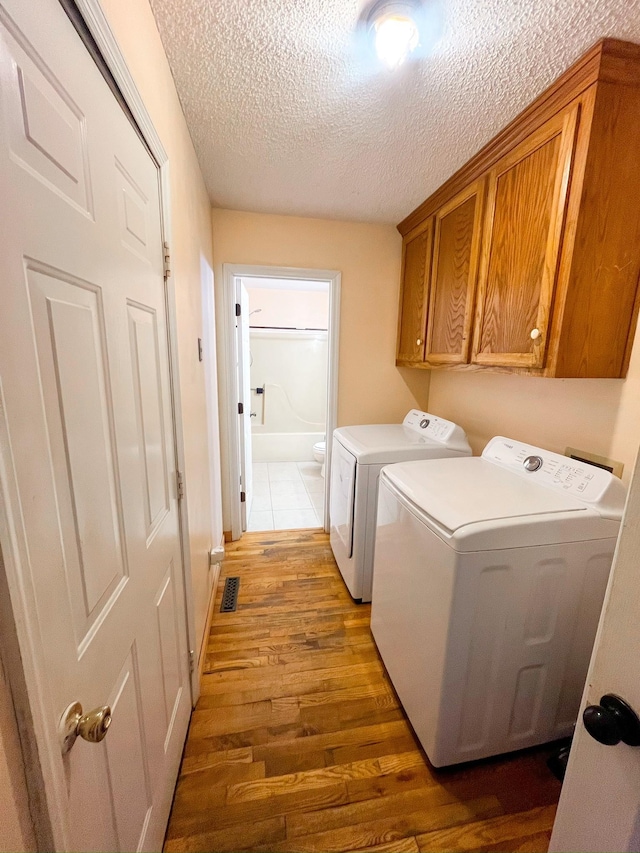 clothes washing area featuring cabinets, separate washer and dryer, a textured ceiling, and dark hardwood / wood-style floors