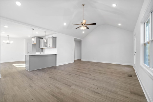 unfurnished living room with ceiling fan with notable chandelier, sink, dark hardwood / wood-style flooring, and vaulted ceiling