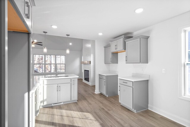 kitchen featuring ceiling fan, gray cabinetry, light wood-type flooring, a large fireplace, and sink