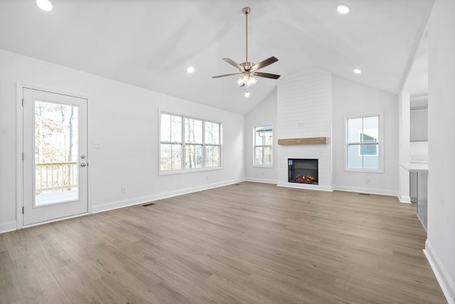 unfurnished living room featuring ceiling fan, a large fireplace, light hardwood / wood-style flooring, and a wealth of natural light