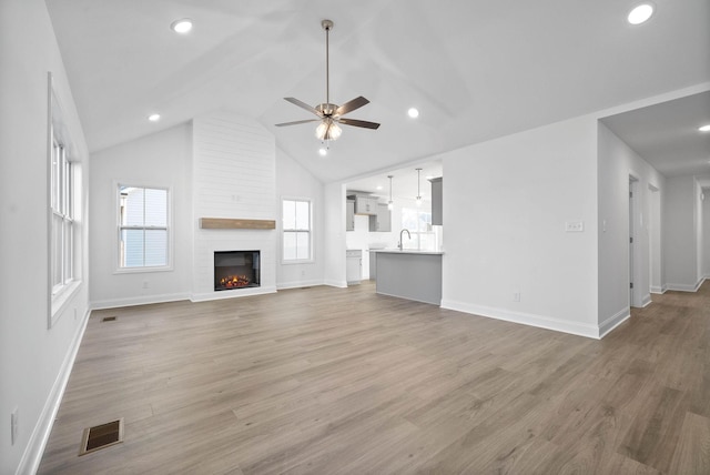 unfurnished living room featuring ceiling fan, a large fireplace, sink, light hardwood / wood-style flooring, and high vaulted ceiling