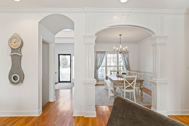 dining area with decorative columns, light hardwood / wood-style flooring, ornamental molding, and an inviting chandelier