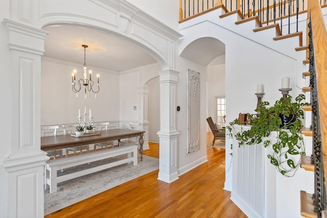 interior space with a notable chandelier, hardwood / wood-style floors, ornate columns, crown molding, and a high ceiling