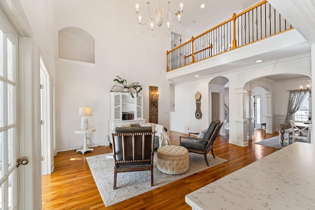 living room featuring hardwood / wood-style floors, a towering ceiling, an inviting chandelier, ornamental molding, and decorative columns