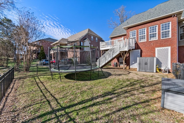 rear view of property with a deck, a yard, and a trampoline