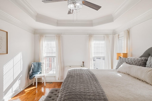 bedroom with ceiling fan, a raised ceiling, crown molding, and wood-type flooring