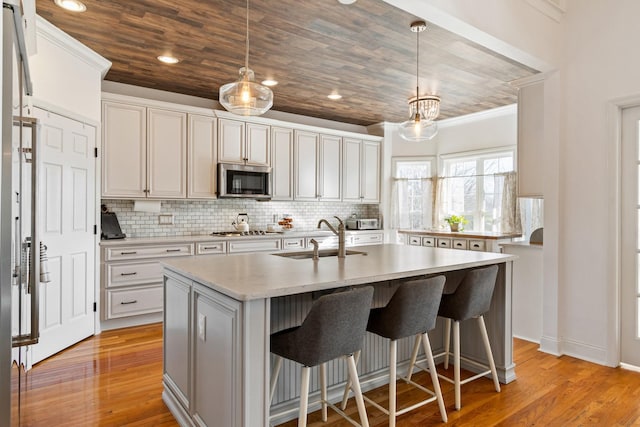 kitchen with appliances with stainless steel finishes, tasteful backsplash, hanging light fixtures, a kitchen island with sink, and sink