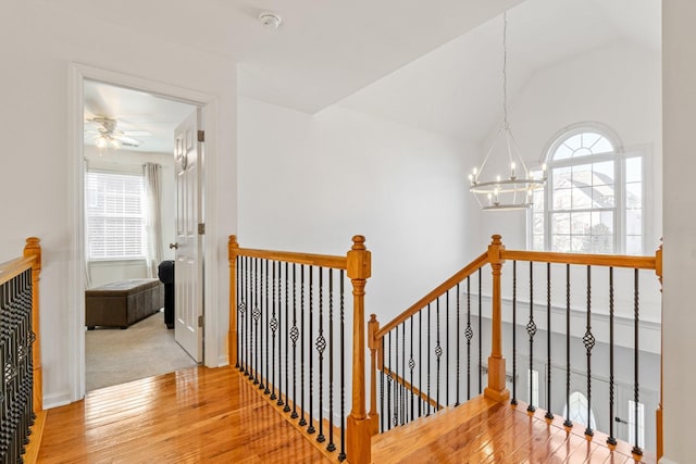 hall with hardwood / wood-style floors, lofted ceiling, and a chandelier