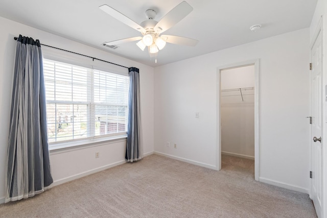 unfurnished bedroom featuring a closet, ceiling fan, a spacious closet, and light carpet