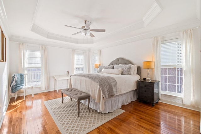 bedroom with ceiling fan, hardwood / wood-style floors, a tray ceiling, and ornamental molding