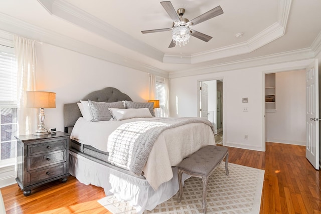 bedroom featuring wood-type flooring, crown molding, ceiling fan, and a raised ceiling