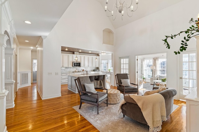 living room featuring a notable chandelier, high vaulted ceiling, light hardwood / wood-style flooring, and sink