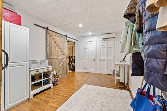 miscellaneous room featuring hardwood / wood-style flooring, a barn door, an AC wall unit, and a drop ceiling