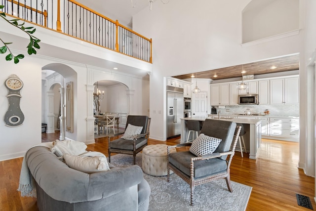 living room featuring sink, a towering ceiling, a notable chandelier, and light wood-type flooring