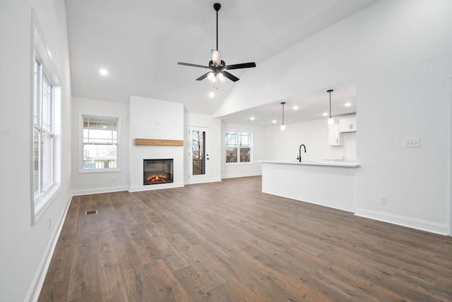 unfurnished living room featuring ceiling fan, sink, a large fireplace, and a healthy amount of sunlight