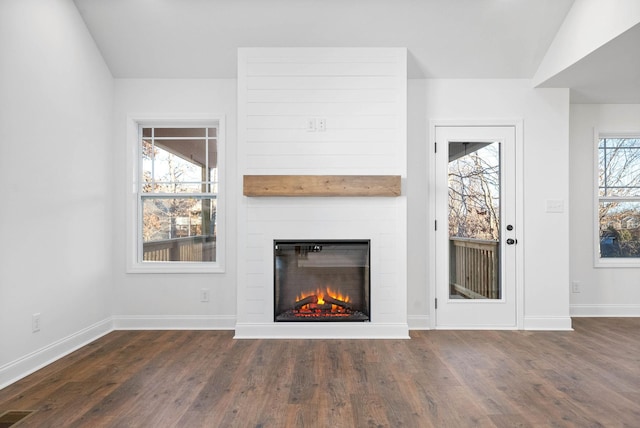 unfurnished living room with dark wood-type flooring, a large fireplace, lofted ceiling, and a healthy amount of sunlight