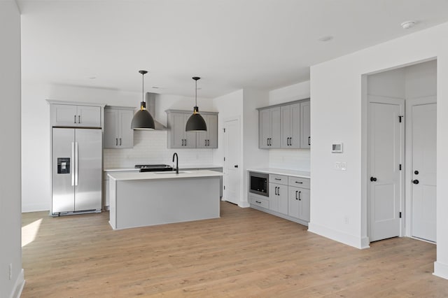 kitchen with stainless steel fridge with ice dispenser, gray cabinets, a kitchen island with sink, built in microwave, and hanging light fixtures