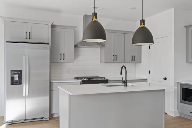 kitchen featuring sink, wall chimney range hood, stainless steel appliances, and an island with sink