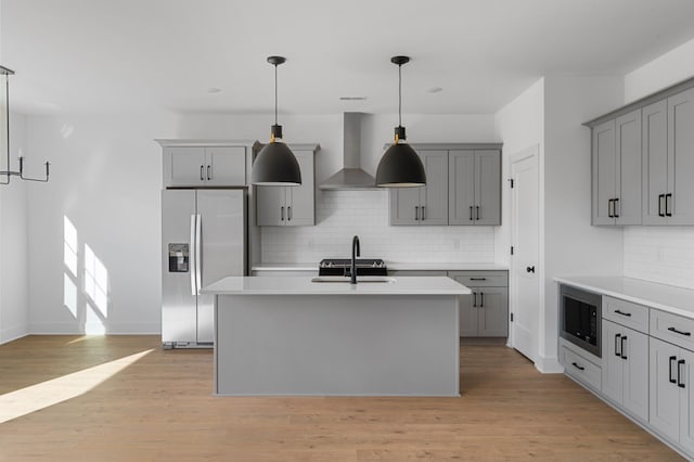 kitchen with pendant lighting, stainless steel refrigerator with ice dispenser, a kitchen island with sink, built in microwave, and wall chimney exhaust hood