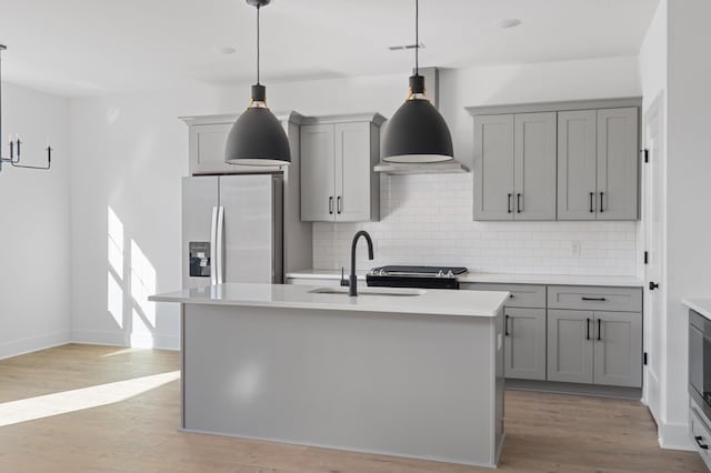 kitchen featuring stainless steel refrigerator with ice dispenser, a center island with sink, and hanging light fixtures