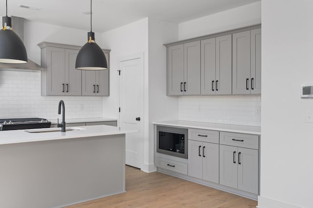 kitchen with hanging light fixtures, sink, wall chimney exhaust hood, and black microwave