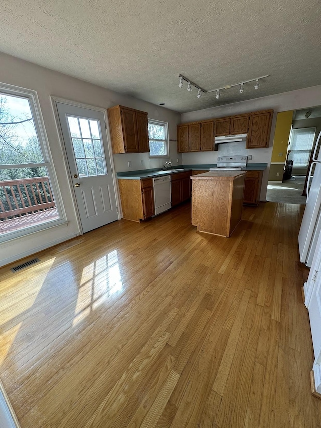 kitchen featuring a center island, sink, white appliances, light wood-type flooring, and a textured ceiling