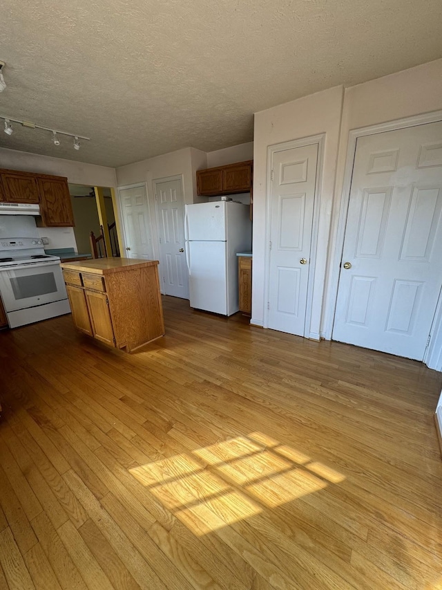 kitchen with a textured ceiling, a kitchen island, light wood-type flooring, and white appliances