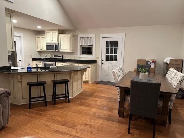 dining space featuring high vaulted ceiling, sink, and light hardwood / wood-style floors