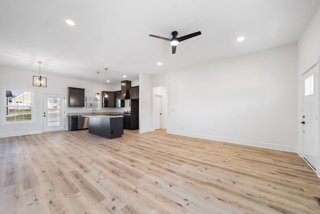 kitchen with ceiling fan, wall chimney range hood, pendant lighting, a kitchen island, and light wood-type flooring