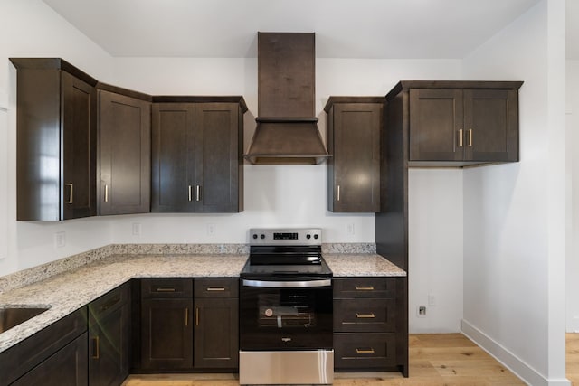 kitchen featuring premium range hood, light hardwood / wood-style floors, electric range, light stone countertops, and dark brown cabinetry