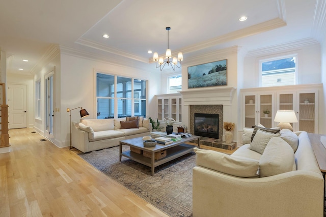 living room with a raised ceiling, a tiled fireplace, an inviting chandelier, and hardwood / wood-style flooring